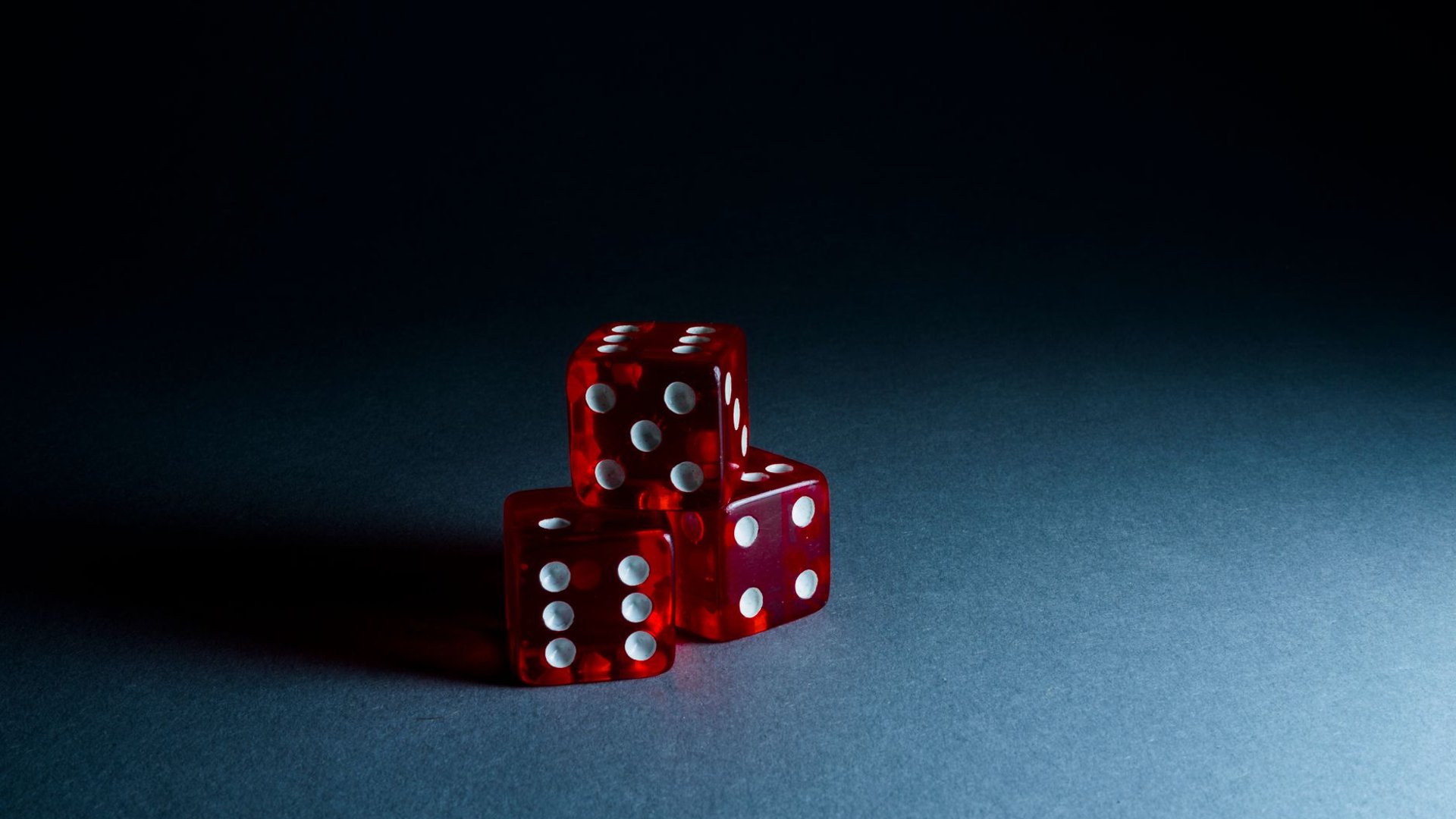 Drei rote Würfel im dunklen Licht, Symbolbild psychologische Risiken beim Glücksspiel