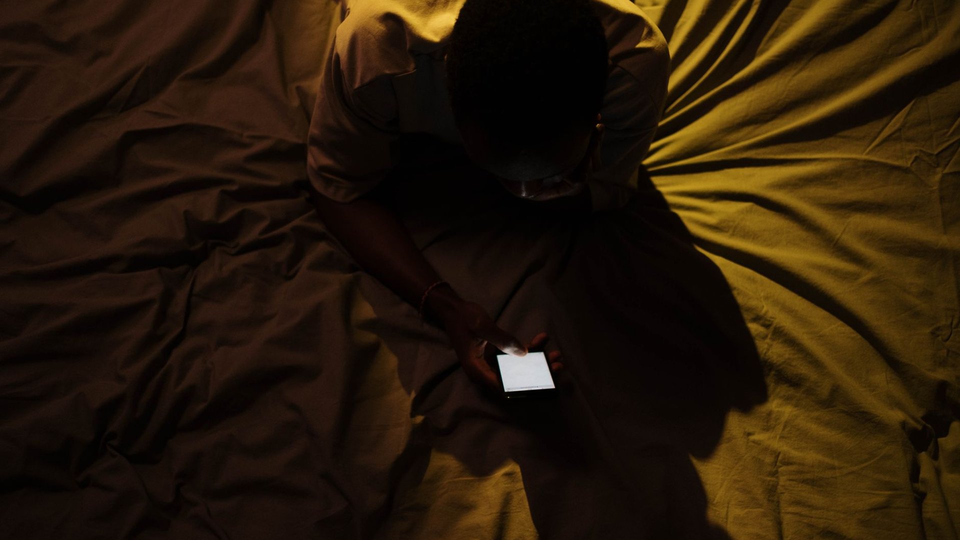 Person nachts allein mit Smartphone im Bett, Symbolbild 24/7-Verfügbarkeit beim Glücksspiel