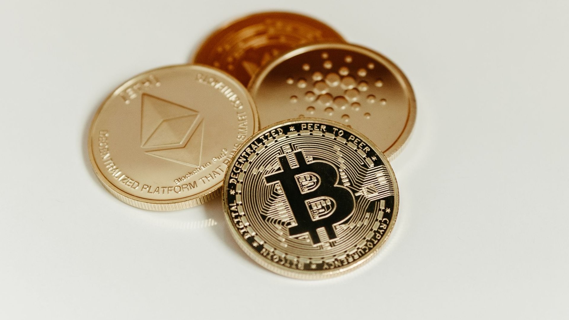 Goldene Bitcoin-, Ethereum- und Cardano-Muenzen als Symbolbild fuer Kryptowaehrungen